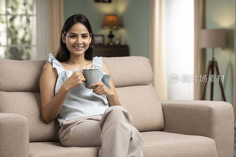 年轻女子坐在沙发上拿着喝咖啡，stock photo